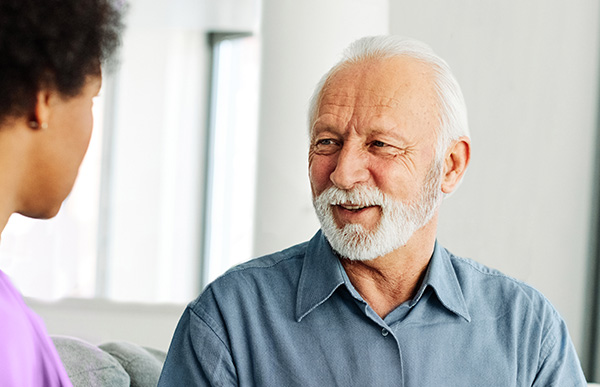 elderly man sitting on couch smiling at caregiver
