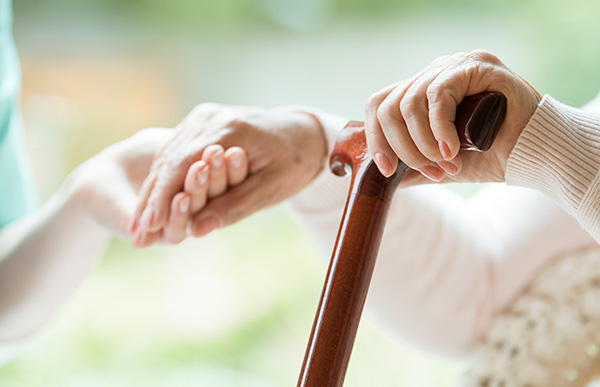 老妇人的手放在拐杖上，被护理人员扶起