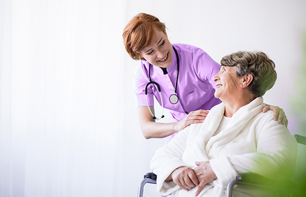 Пожилая женщина в белом халате сидит в кресле и улыбается медсестре