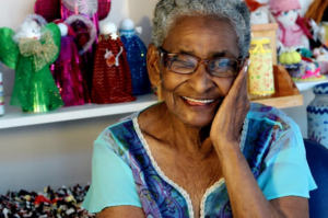 a smiling woman poses with a doll collection – Amazing Home Care