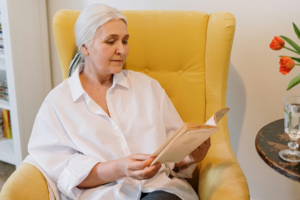 an older woman reads a book in a yellow chair – Nestfully
